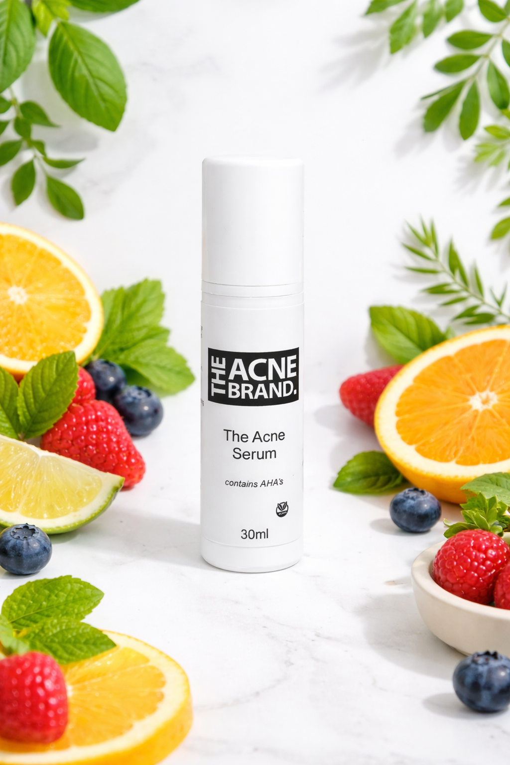 The Acne Serum from the plant-based acne skincare range on a marble surface with fruits and leaves.